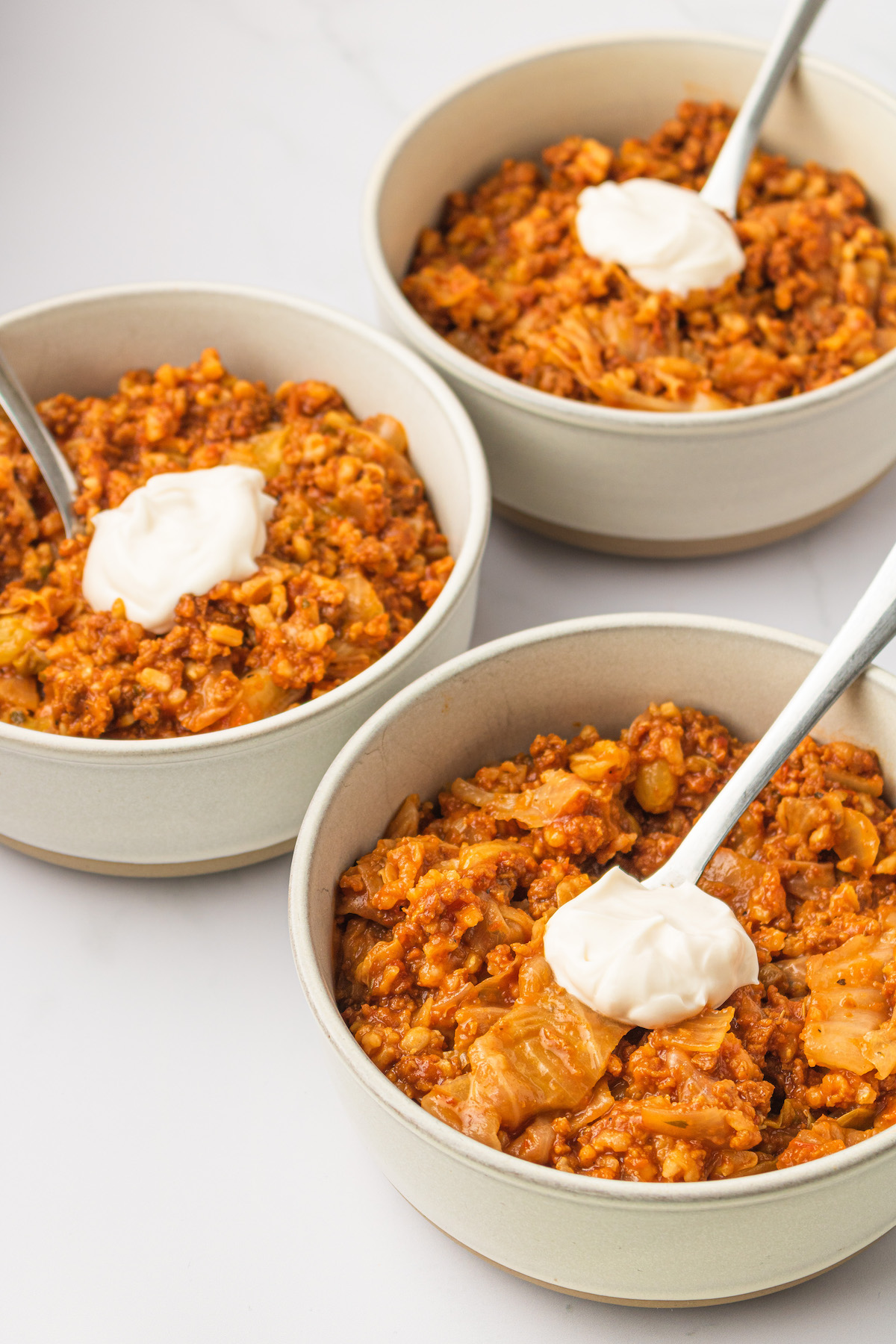 3 bowls of vegan unstuffed cabbage rolls with spoons and sour cream on top