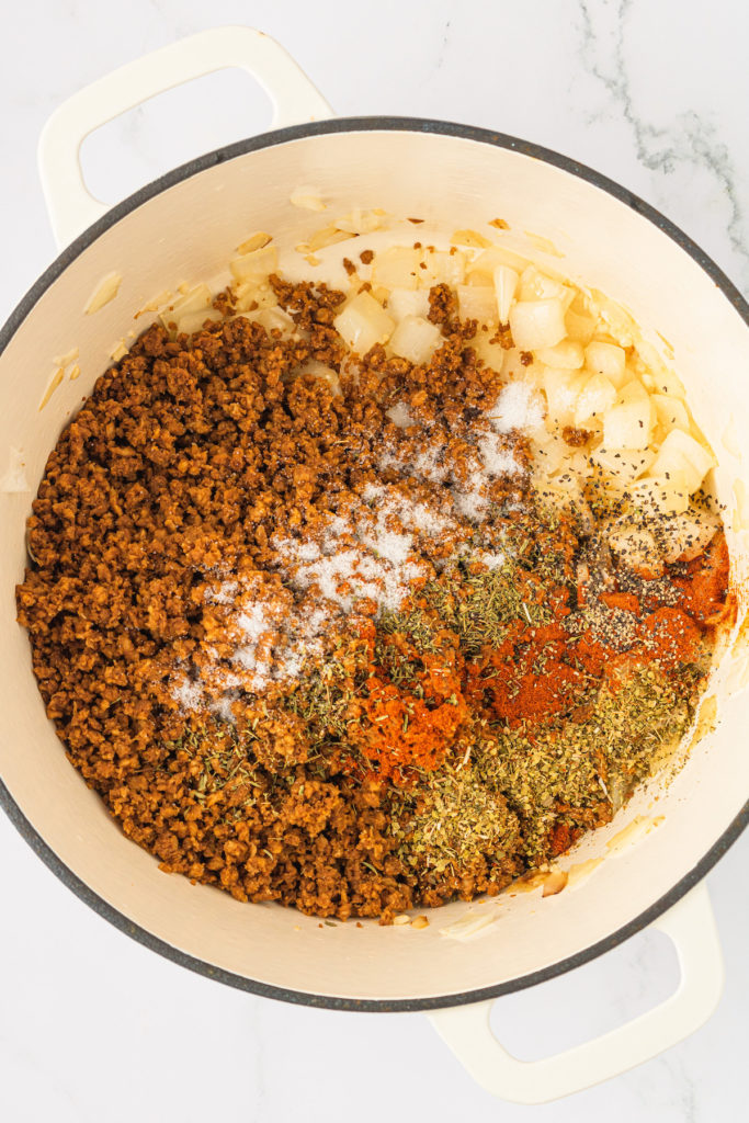 Overhead view of onions, vegan ground beef, and seasonings in Dutch oven