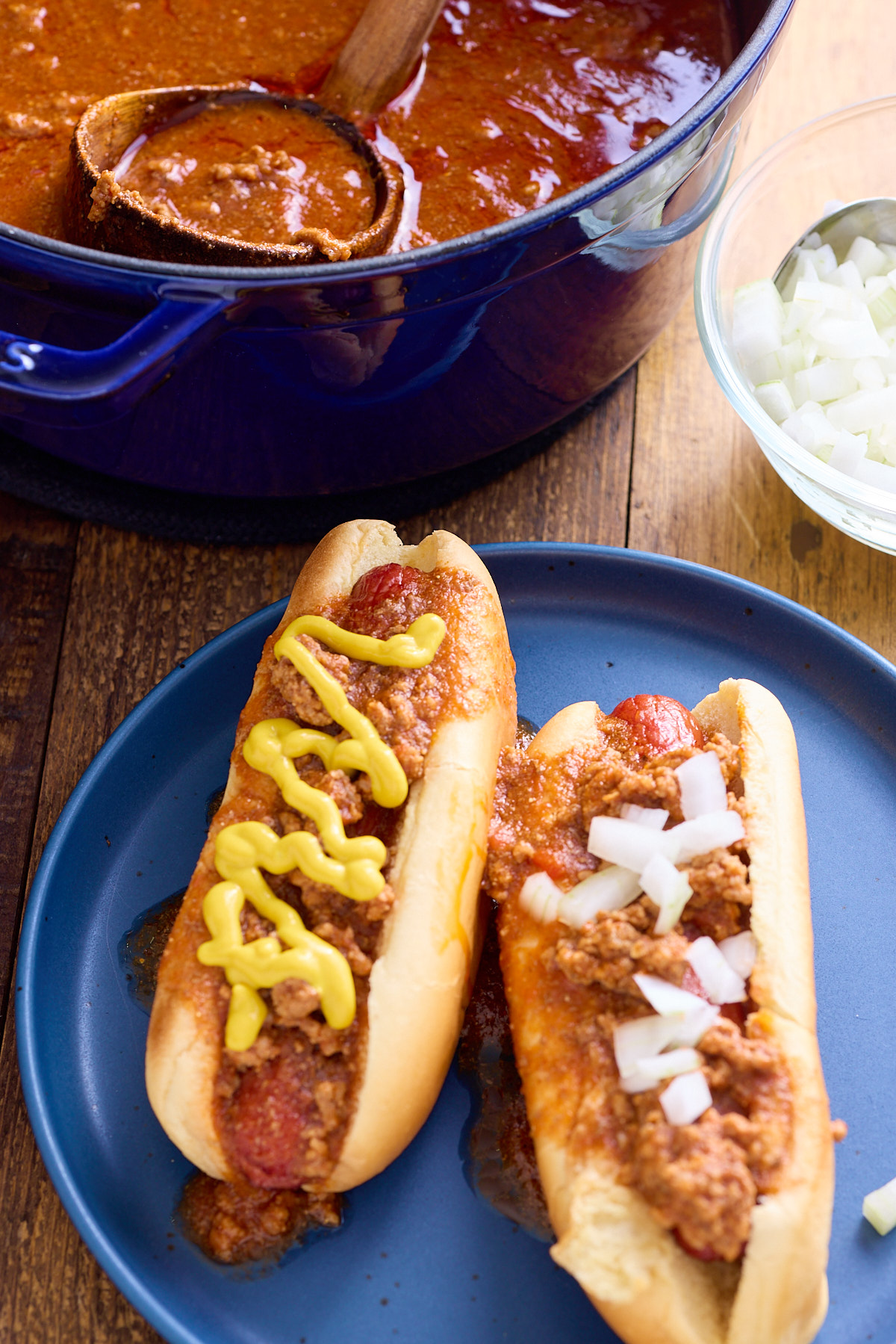 chili hot dogs with mustard and hot dogs on them with pot of hot dog chili in back