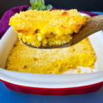 scalloped corn in a baking dish with a wooden spoon