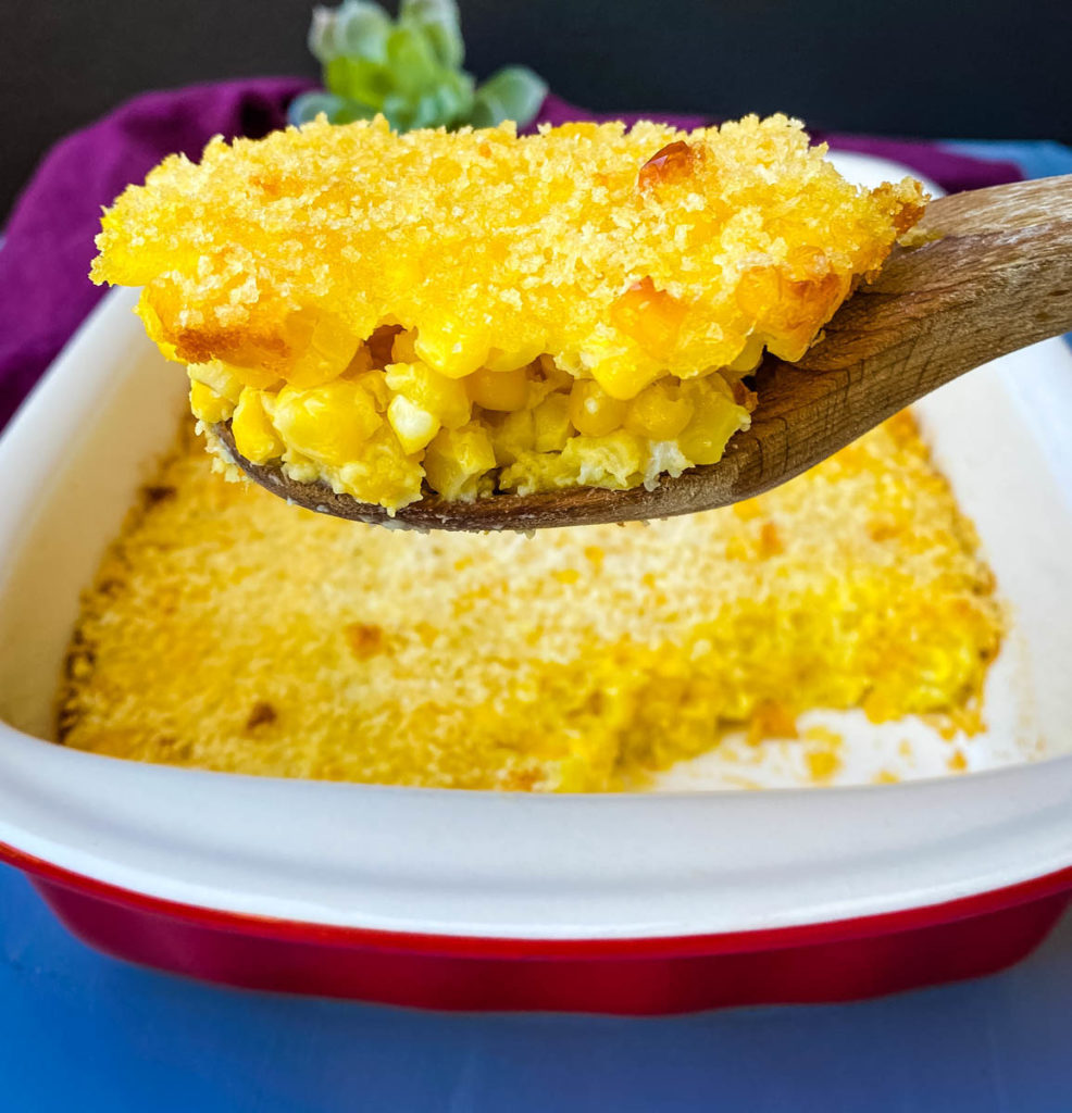 scalloped corn in a baking dish with a wooden spoon