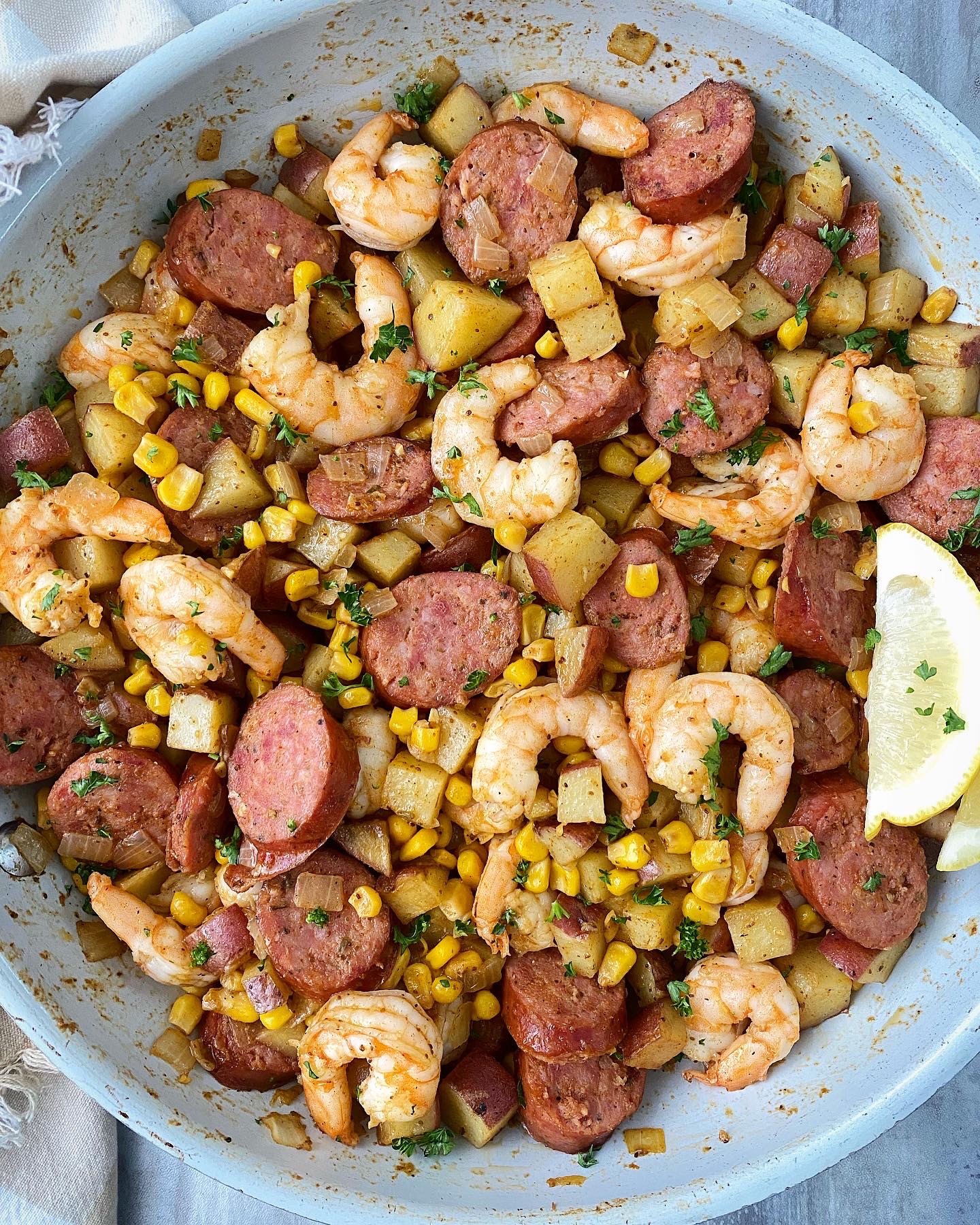 overhead shot of shrimp boil in a white skillet garnished with fresh parsley