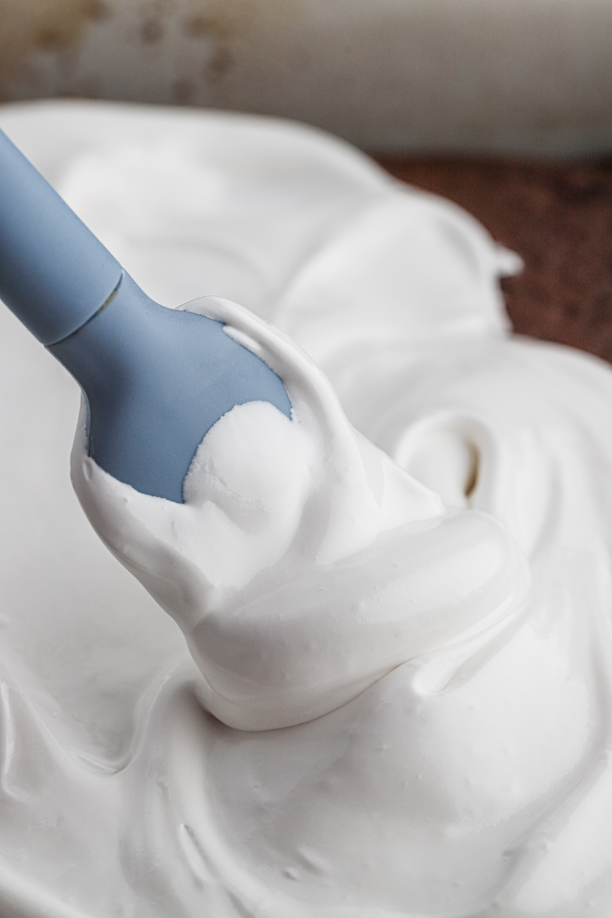 A blue rubber spatula in a bowl of seven minute frosting.