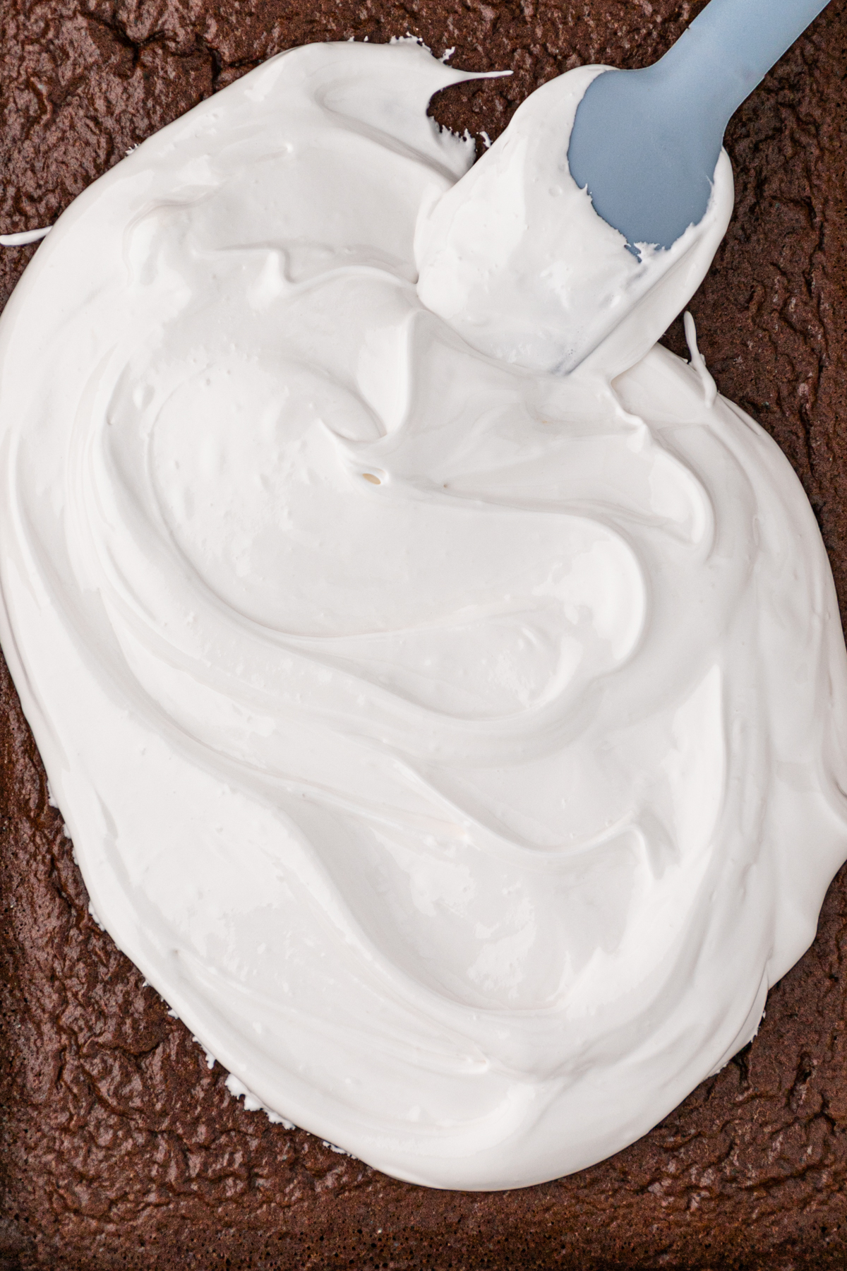 A blue spatula spreading seven minute frosting on a cake.