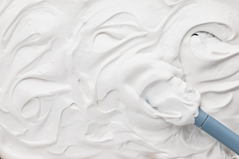 A blue spatula spreading seven minute frosting on a cake.