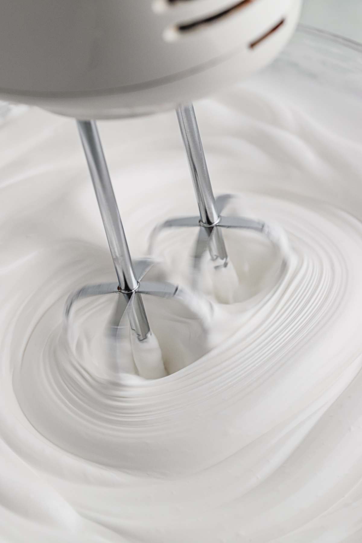 A hand mixer in a bowl of seven minute frosting.