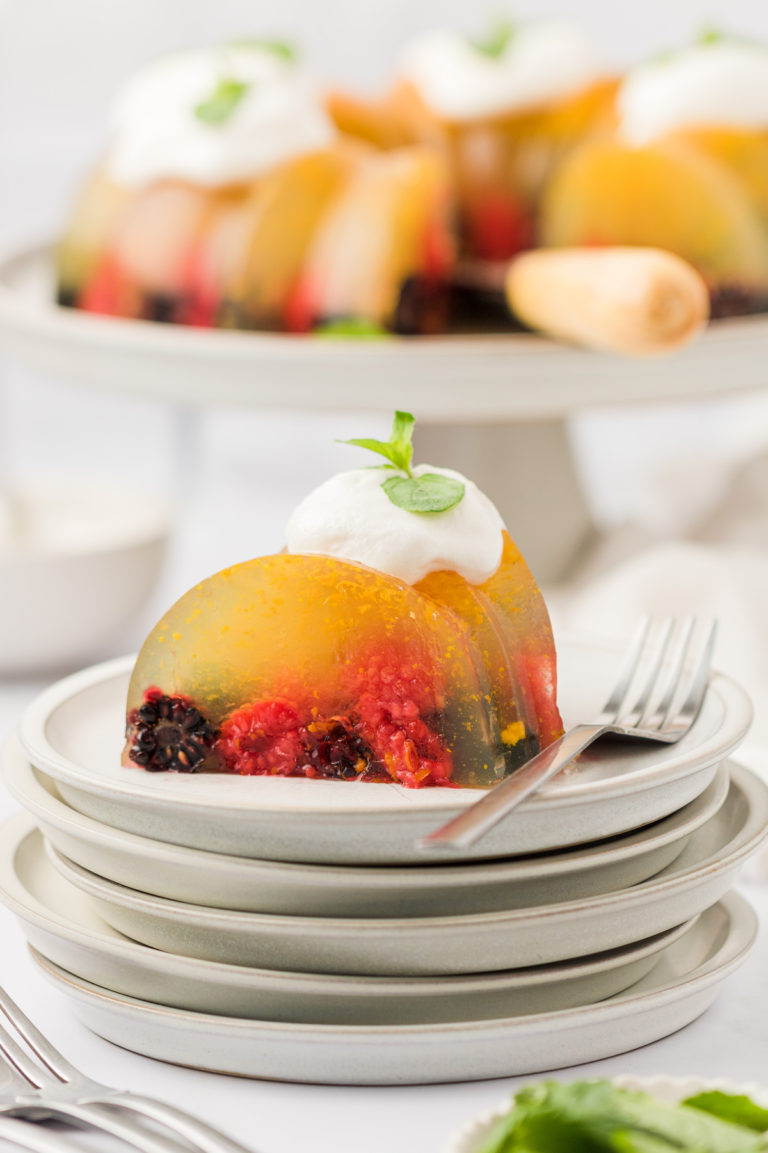 Slice of vegan congealed fruit salad on a plate with dollop of whipped cream and sprig of mint