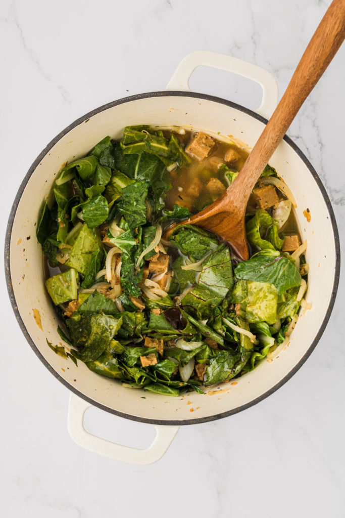Wooden spoon stirring turnip greens in pot