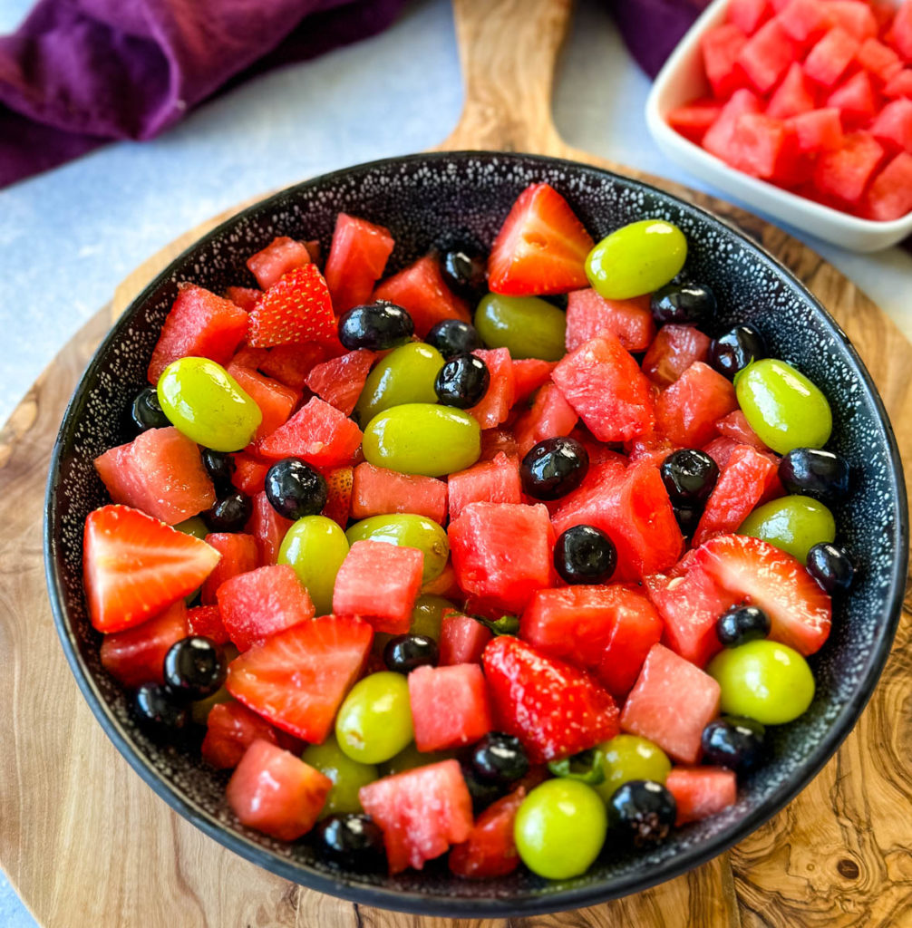 watermelon fruit salad with strawberries, blueberries, grapes, and basil in a black bowl