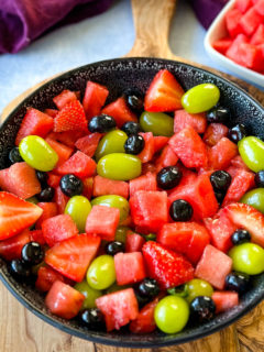 watermelon fruit salad with strawberries, blueberries, grapes, and basil in a black bowl