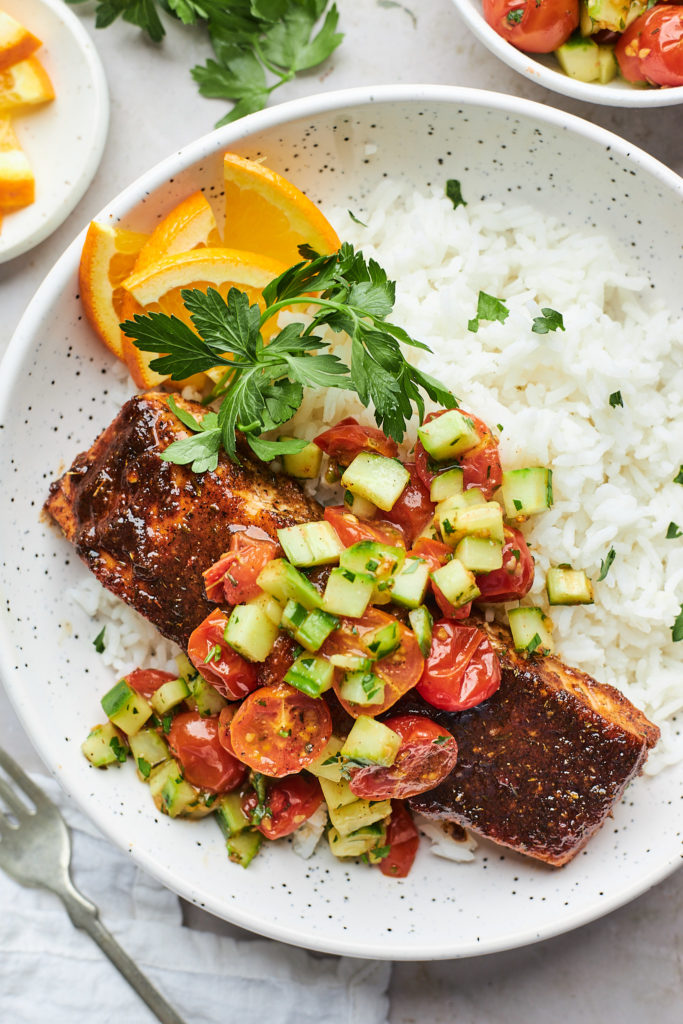 A delicious jerk salmon on white rice with tomato salad on top