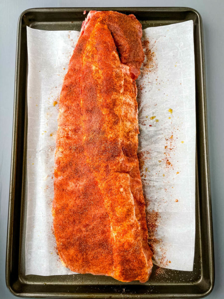 raw seasoned rack of pork ribs on a parchment paper lined sheet pan