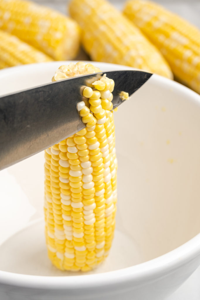 Knife slicing kernels from ear of corn