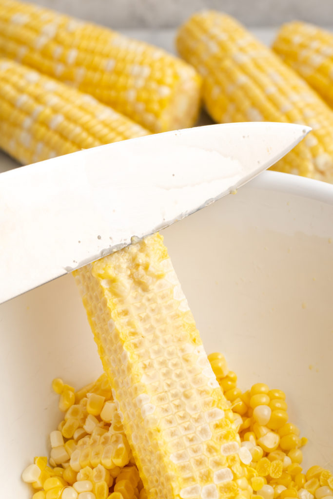 Knife slicing corn from cob into bowl