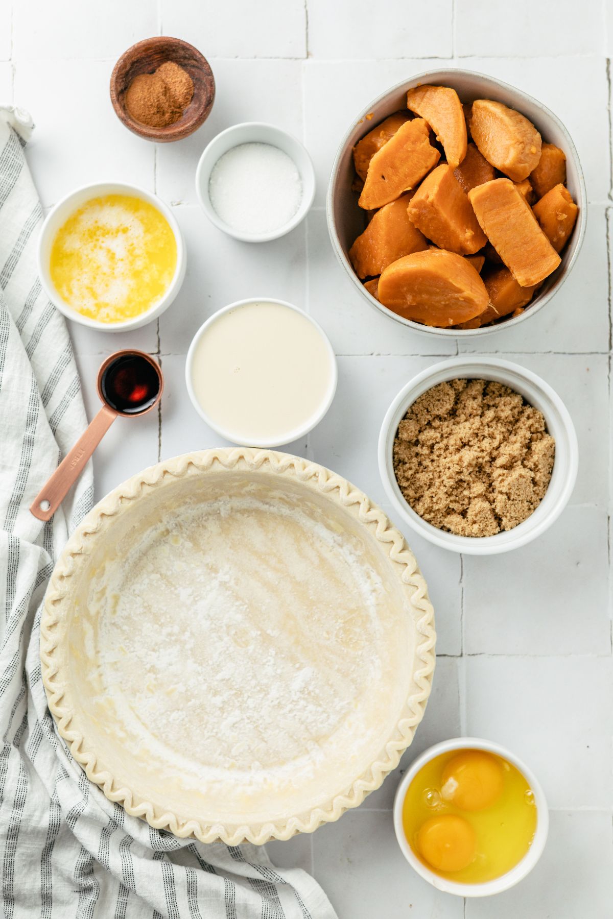 ingredients needed to make canned yams sweet potato pie like: frozen pie crust in an aluminum pie plate, canned sweet potatoes, melted butter, brown sugar, white sugar, evaporated milk eggs, cinnamon, nutmeg, vanilla extract in separate containers