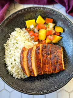 Cajun chicken breast sliced into strips on a plate with white rice and mango salsa