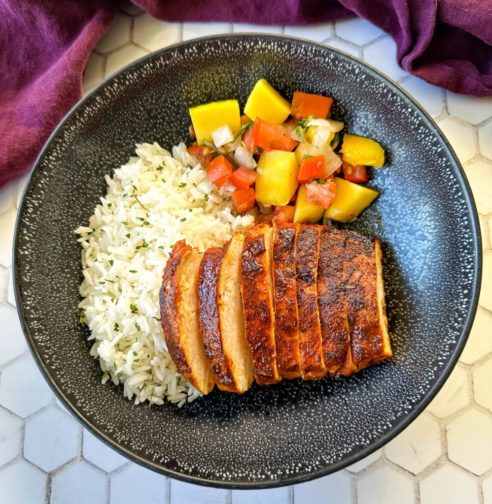 Cajun chicken breast sliced into strips on a plate with white rice and mango salsa