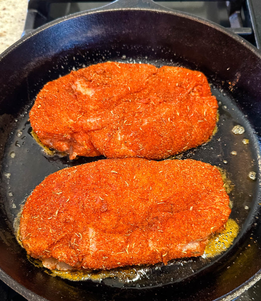 raw seasoned chicken breasts in a cast iron skillet