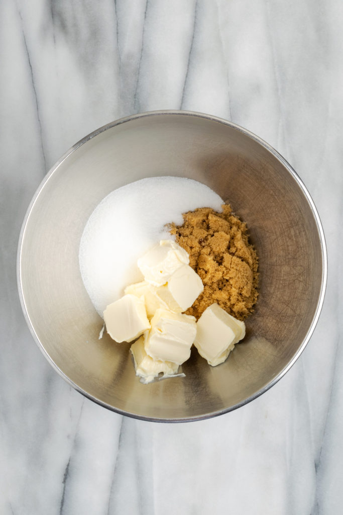 Overhead view of vegan butter, white sugar, and brown sugar in metal mixing bowl