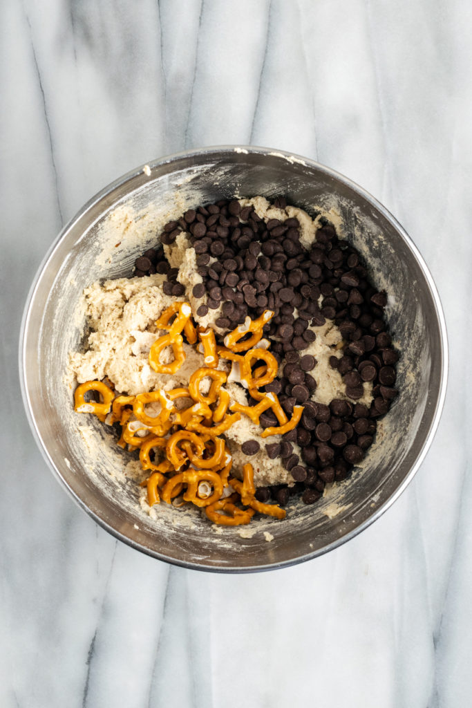 Overhead view of pretzels and chocolate chips added to bowl of cookie dough