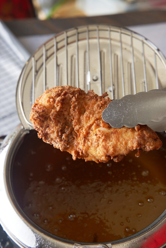 chicken being pulled from oil with tongs