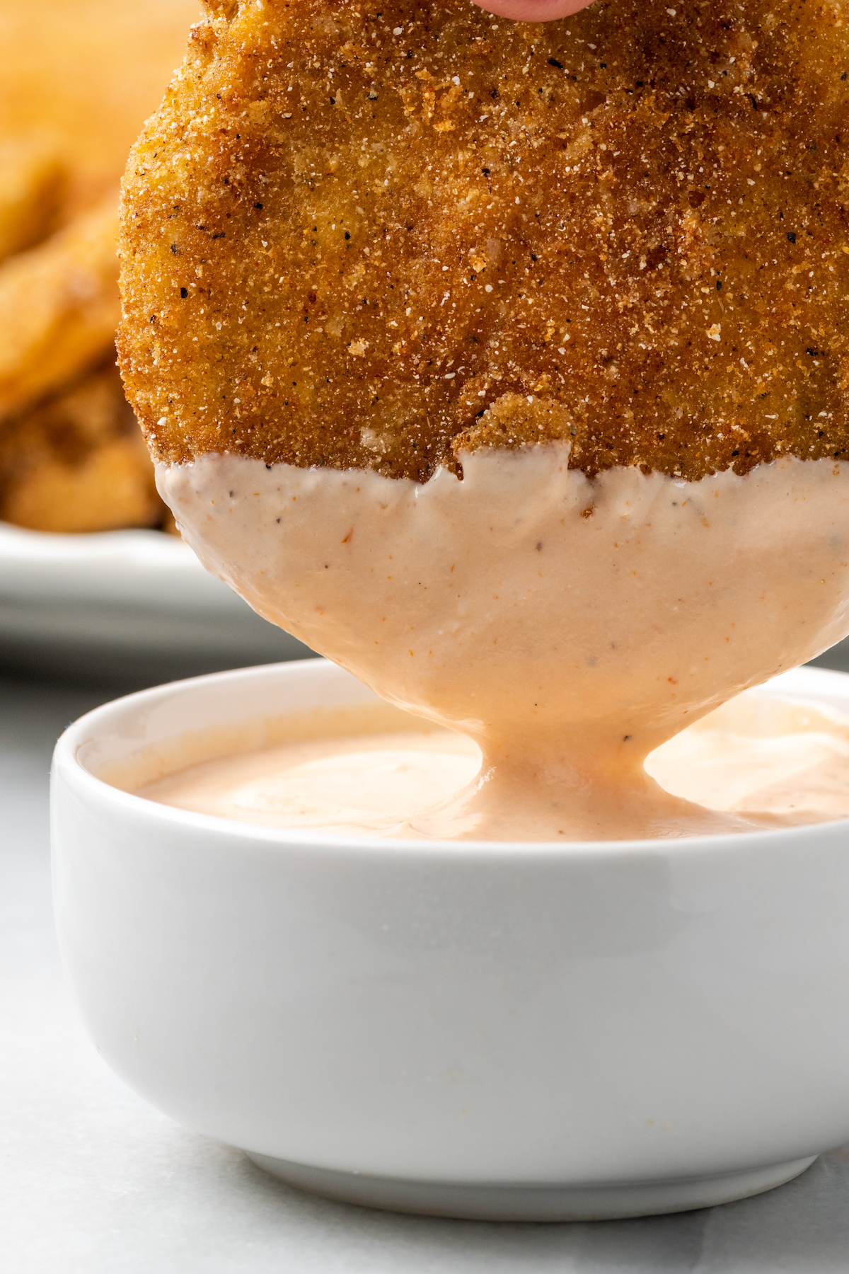 Dipping fried green tomato in small bowl of comeback sauce