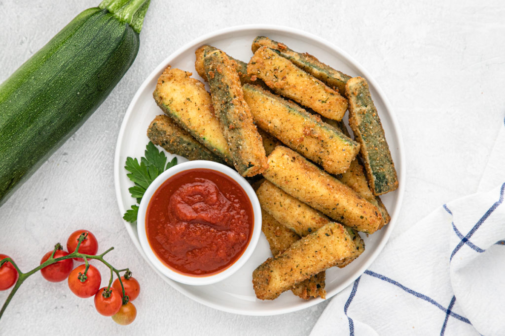 Fried zucchini wedges on a white plate with marinara sauce to serve