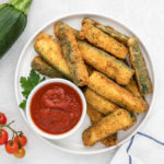 Fried zucchini wedges on a white plate with marinara sauce to serve