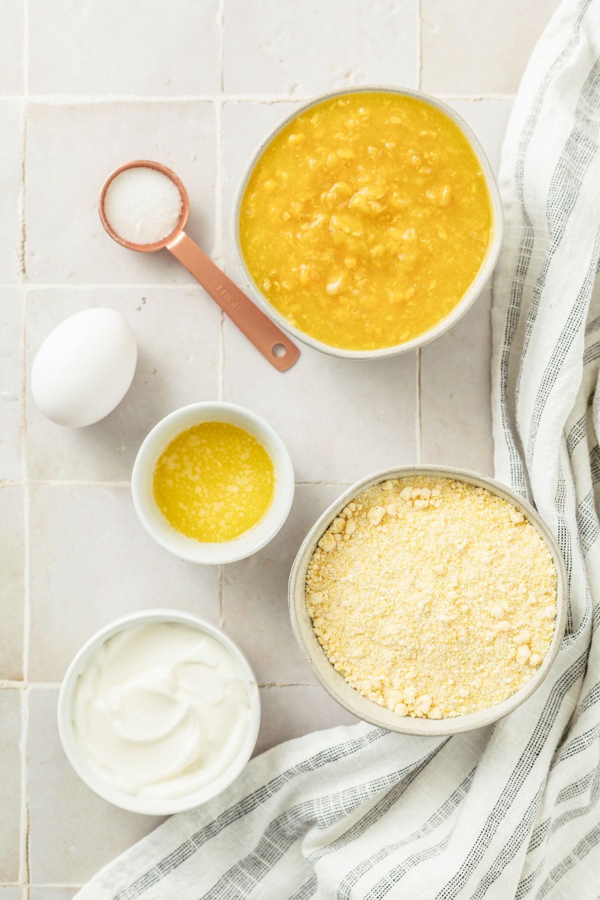 ingredients to make the best jiffy cornbread recipe with creamed corn: Jiffy corn muffin mix, sugar, melted butter, egg, sour cream, and creamed corn in separate bowls