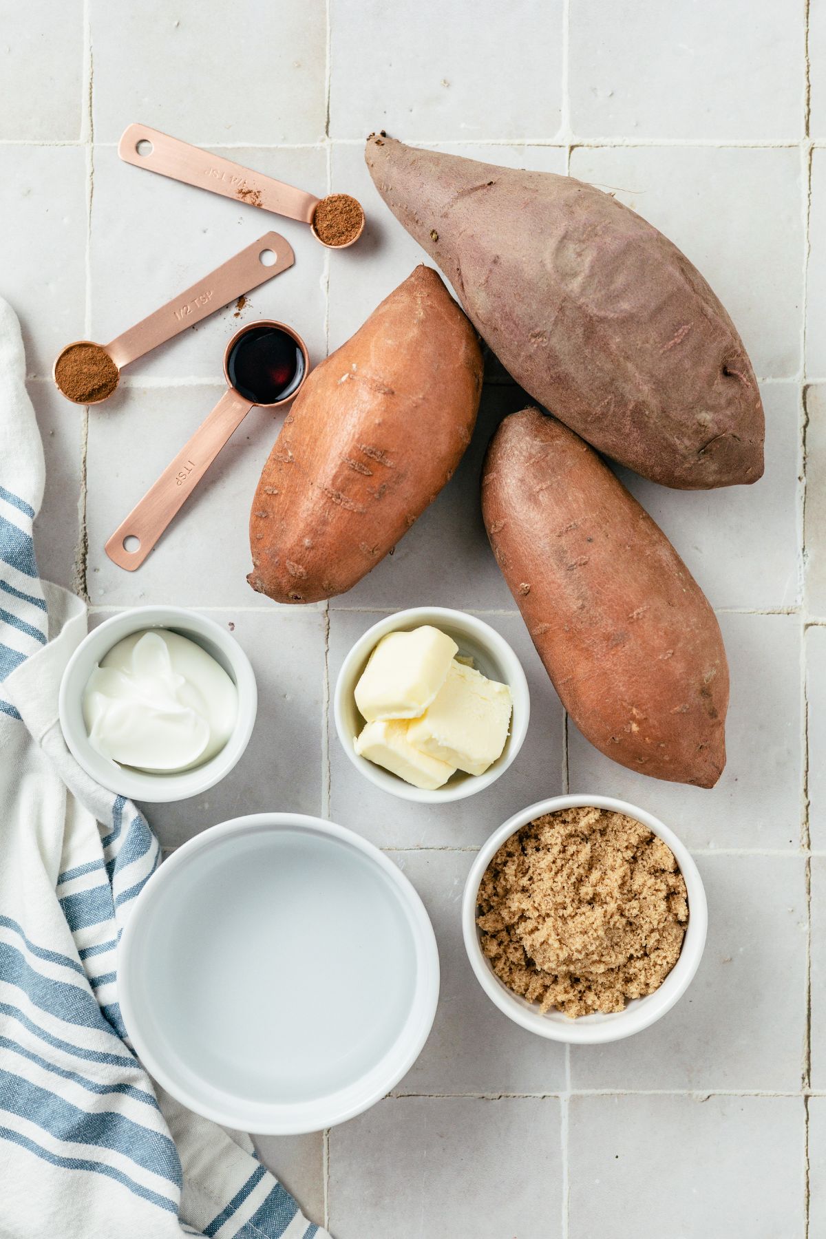 ingredients needed to make whipped sweet potatoes: sweet potatoes, water, butter, vanilla extract, nutmeg, cinnamon, brown sugar and sour cream on separate bowls and spoons