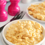 slow cooker mac and cheese in a white bowl with salt and pepper shakers and forks