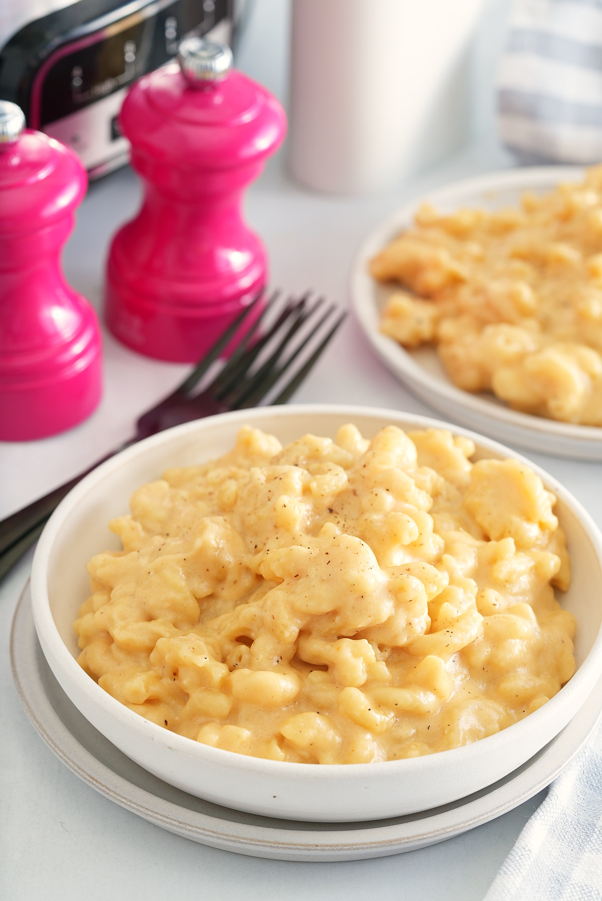 slow cooker mac and cheese in a white bowl with salt and pepper shakers and forks