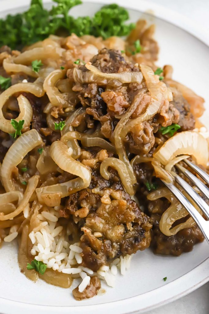 A fork piercing into a liver and onions recipe served over rice