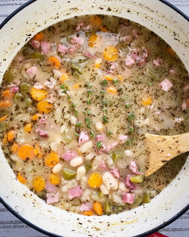overhead shot of cooked ham and been soup in a pot with a wooden spoon