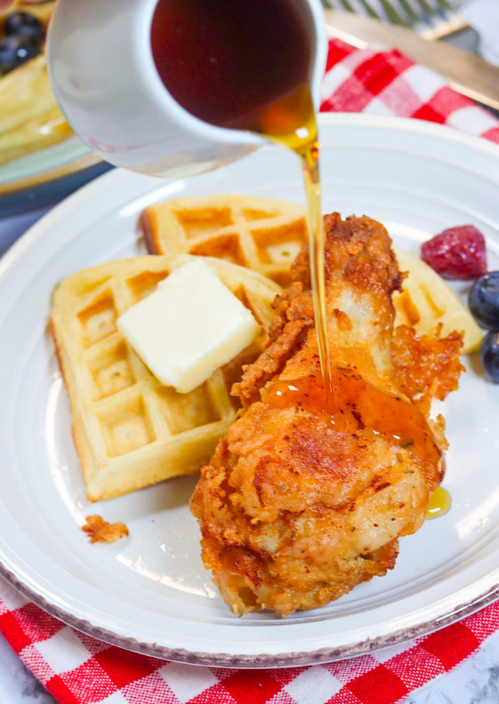 Drizzling maple syrup over fried chicken and waffles