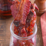 candied bacon in jar with maply syrup in background