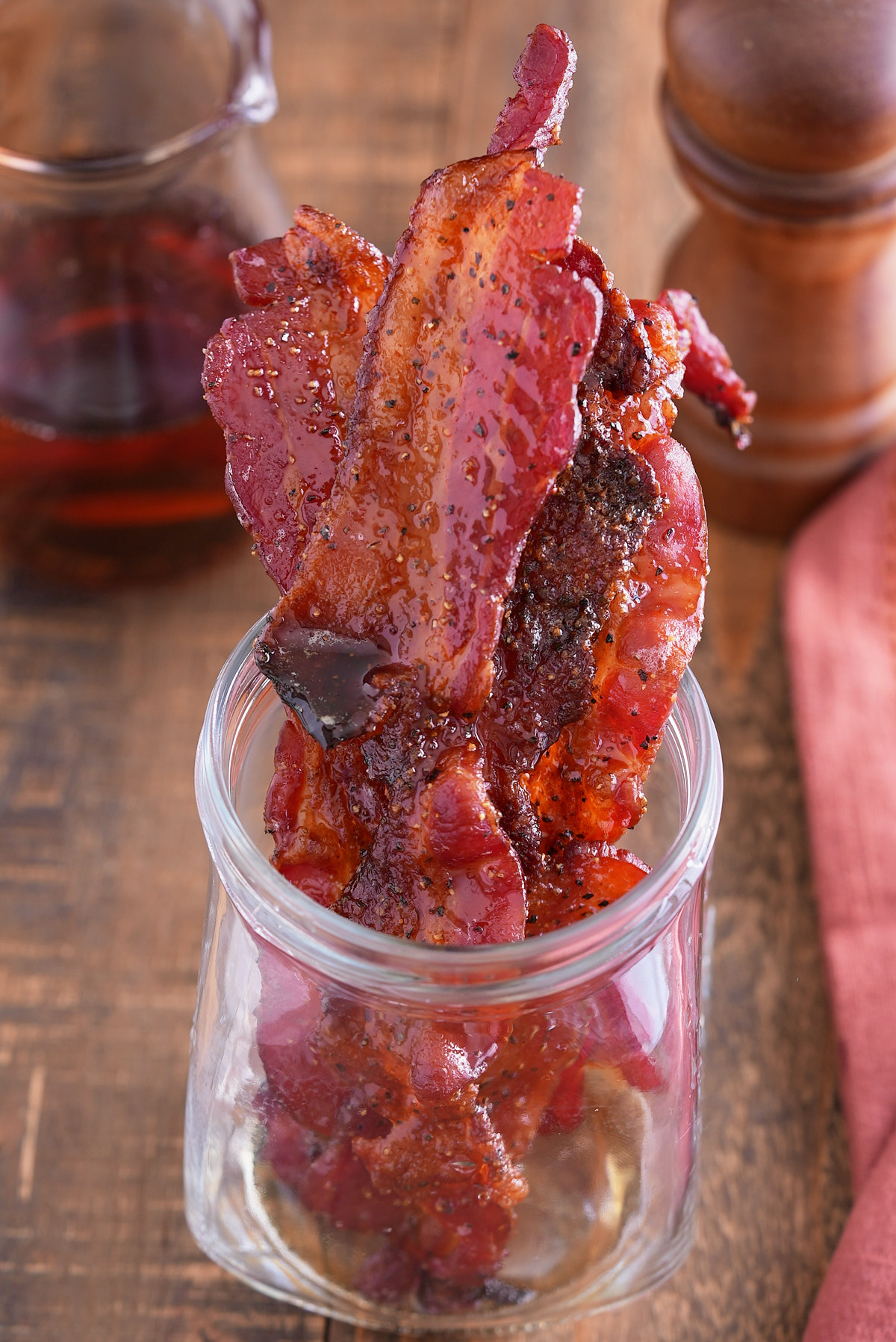 candied bacon in jar with maply syrup in background