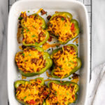 Overhead view of stuffed green peppers in white casserole dish set on wire rack