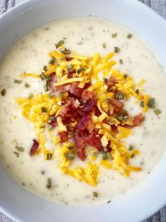 close up of potato soup in a white bowl garnished with bacon, cheddar cheese, and dried chives