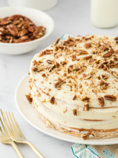 A butter pecan layer cake frosted on a white plate with gold forks