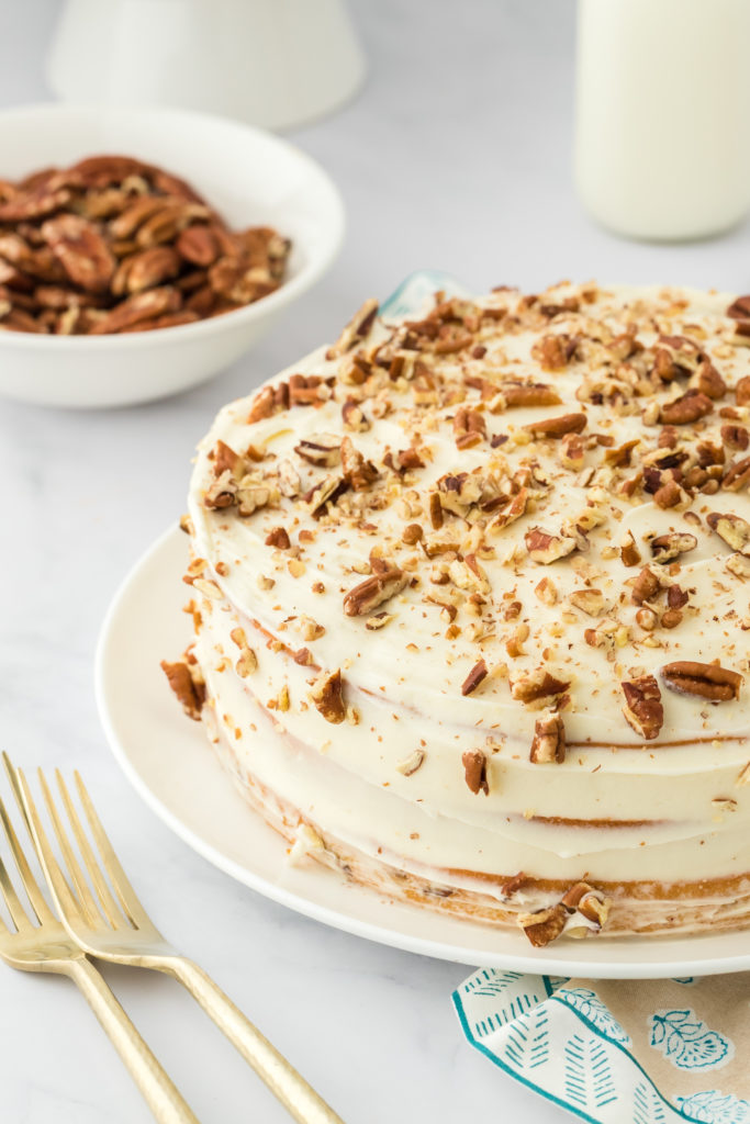 A butter pecan layer cake frosted on a white plate with gold forks