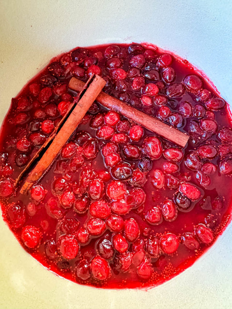 homemade cranberry sauce in a Dutch oven with cinnamon sticks
