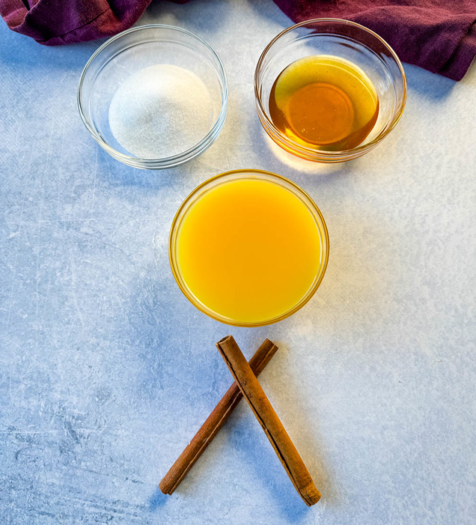 sugar, honey, orange juice, and cinnamon sticks on a flat surface