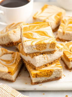 Stack of pumpkin pie cheesecake bars on cutting board with cup of coffee