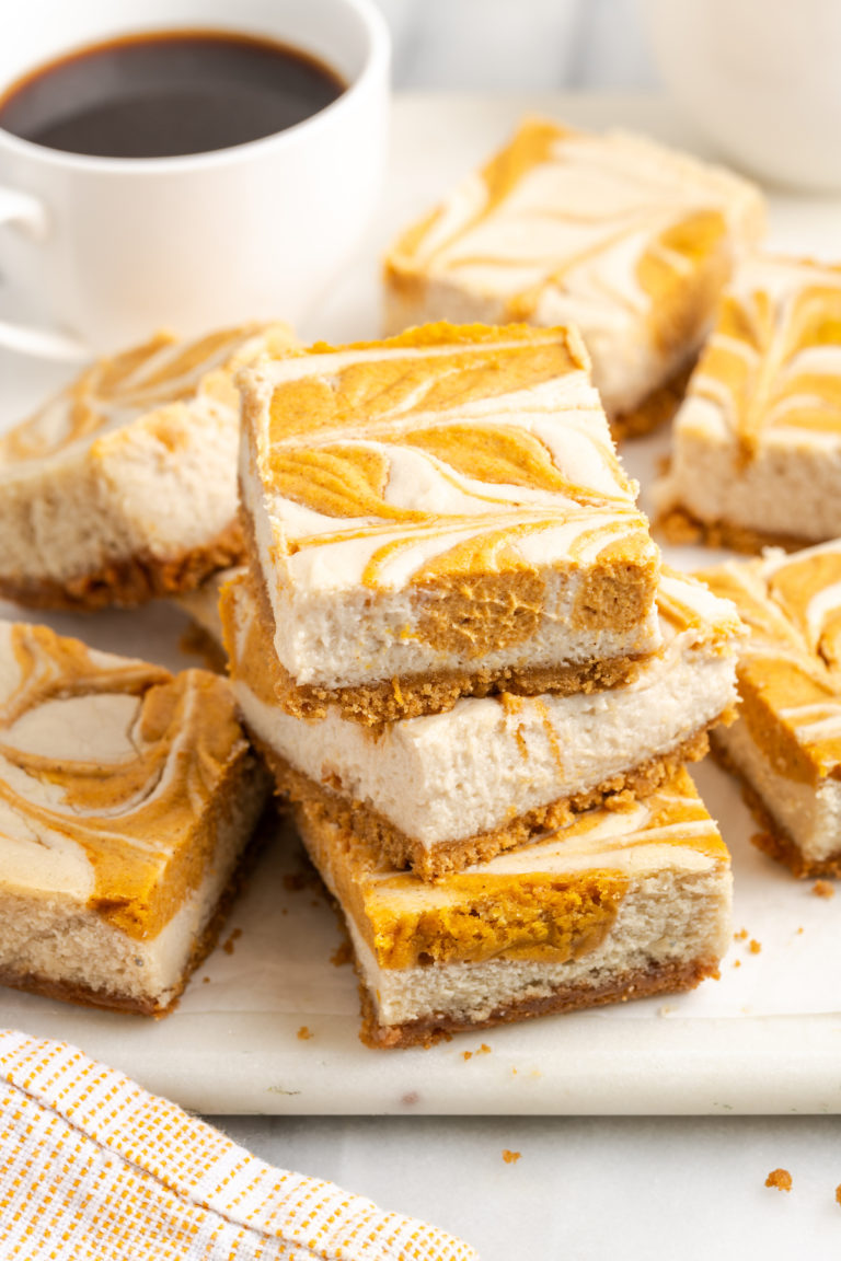 Stack of pumpkin pie cheesecake bars on cutting board with cup of coffee