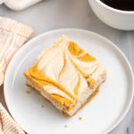pumpkin pie cheesecake bar on white plate next to cup of coffee