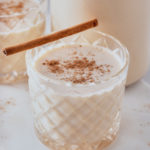 coquito in a glass with nutmeg sprinkled on top and a cinnamon stick on side