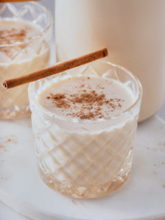 coquito in a glass with nutmeg sprinkled on top and a cinnamon stick on side