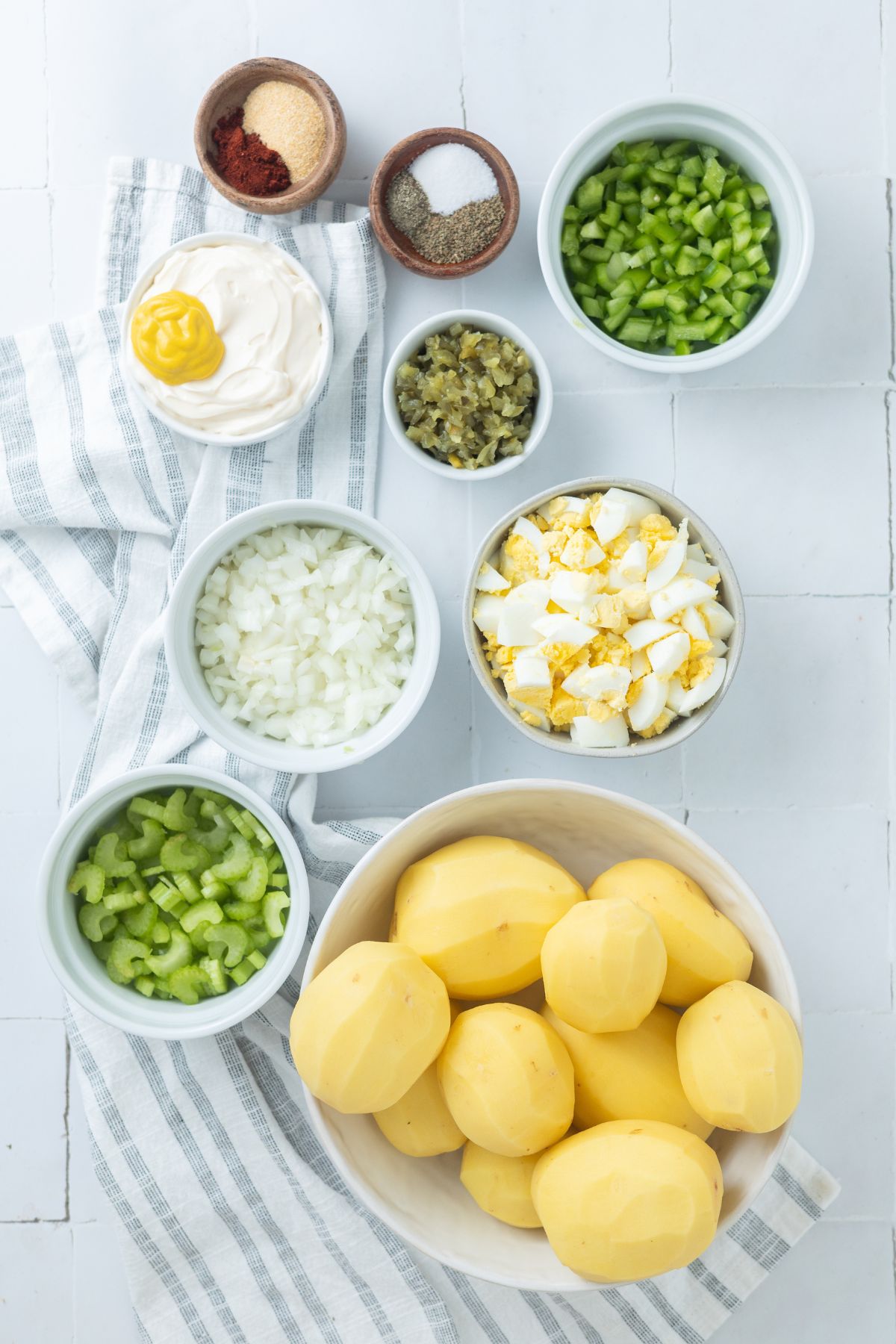 Separate bowls with ingredients for instant pot Potato Salad: Yukon Gold Potatoes, large eggs, yellow onion, green bell pepper, celery, celery seed, mayonnaise, yellow mustard, sweet relish, sea salt, black pepper, smoked paprika, and garlic powder.