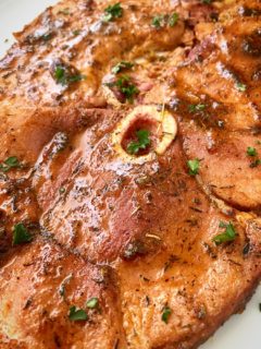 close up show of shot of cooked ham steak on a white plate garnished with fresh parsley